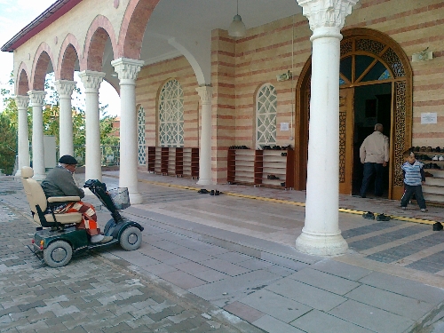 Akülü arabasıyla cami kapısından cemaate katılıyor